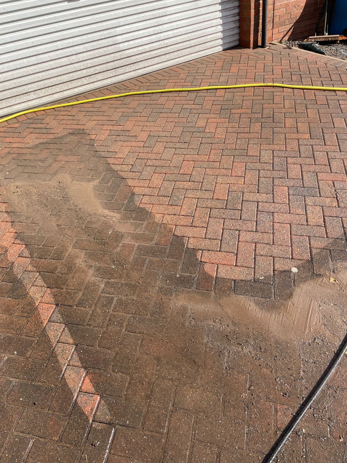 Block paving driveway part-way through pressure washing, showing a clear clean and dirty comparison